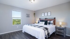 Ein Schlafzimmer mit einem großen Bett, einem Nachttisch mit Lampe, einem Fenster mit Blick und einer Wand mit gerahmten Bildern.