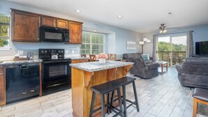 A modern kitchen with dark wooden cabinets, a black microwave, and a built-in oven. There is a large island with bar stools, and a seating area with a gray sofa and a TV. - 2BR Condo | Lake Views | Walk-In Access (Branson)
