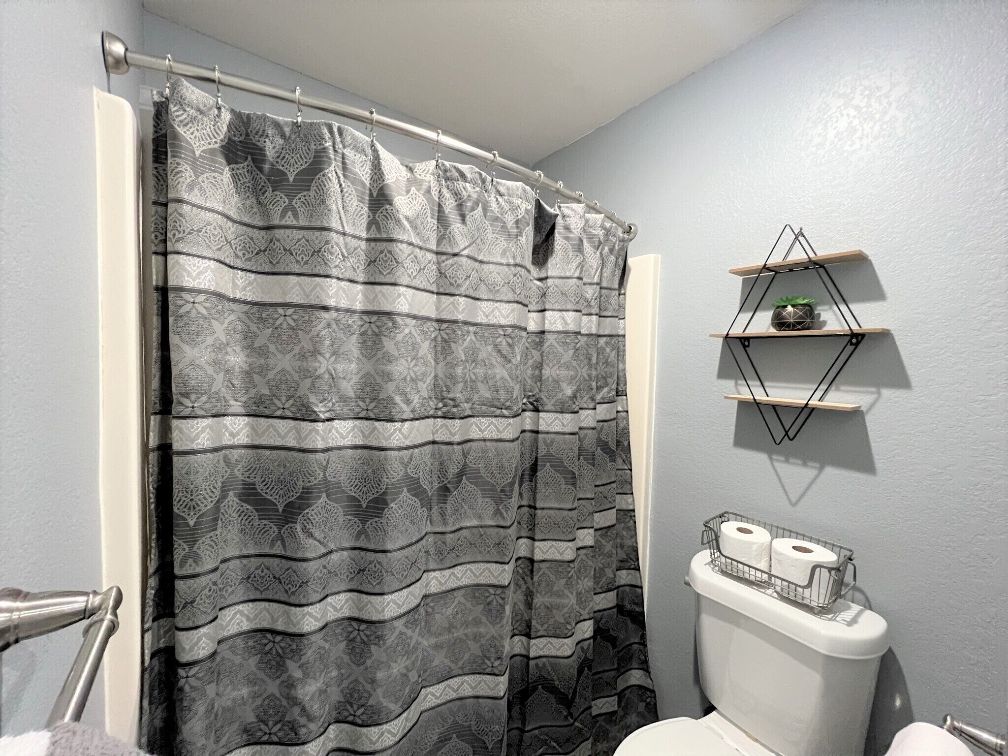 A bathroom with a shower curtain, a toilet, and a shelf with toiletries.