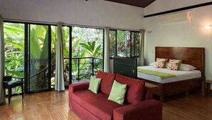 Ein geräumiges Zimmer mit einem roten Sofa, einem Bett mit Holz Kopfteil und einer großen Schiebeglastür, die zu einem üppigen Garten führt.