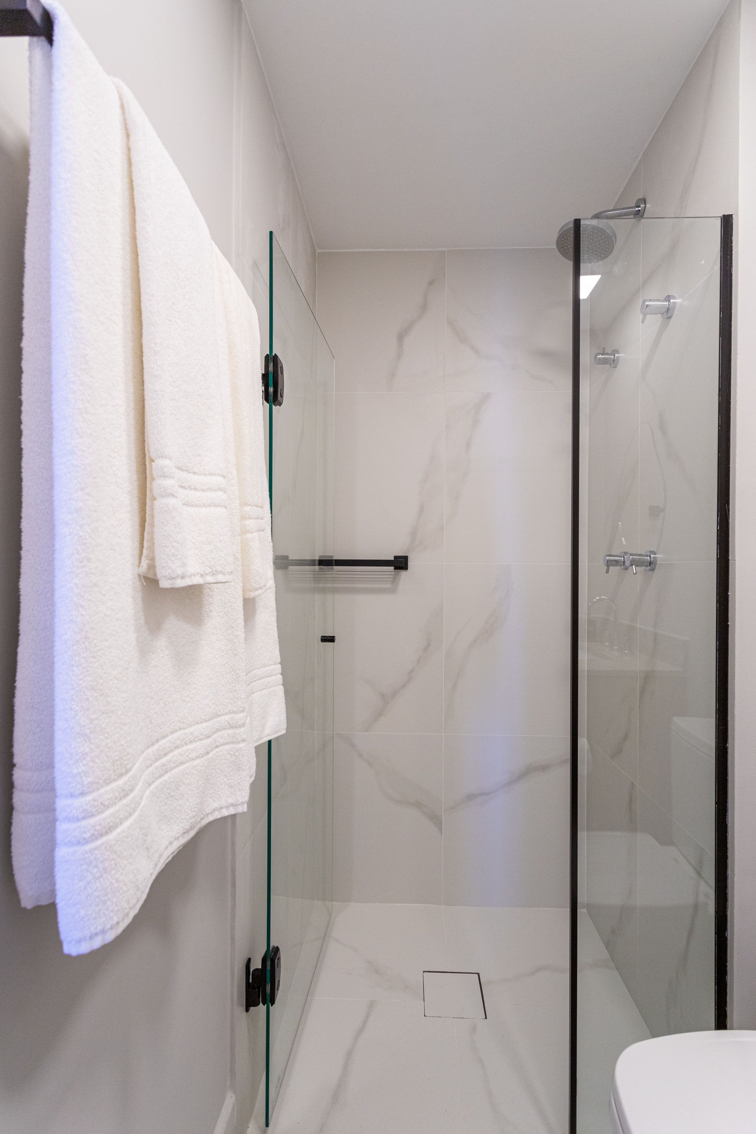 Un baño moderno con ducha envuelta en vidrio, baldosas de mármol blanco y un perchero para toallas.
