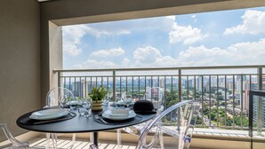 Un balcon avec une table dressée pour le dîner, des chaises transparentes et une vue sur la ville.