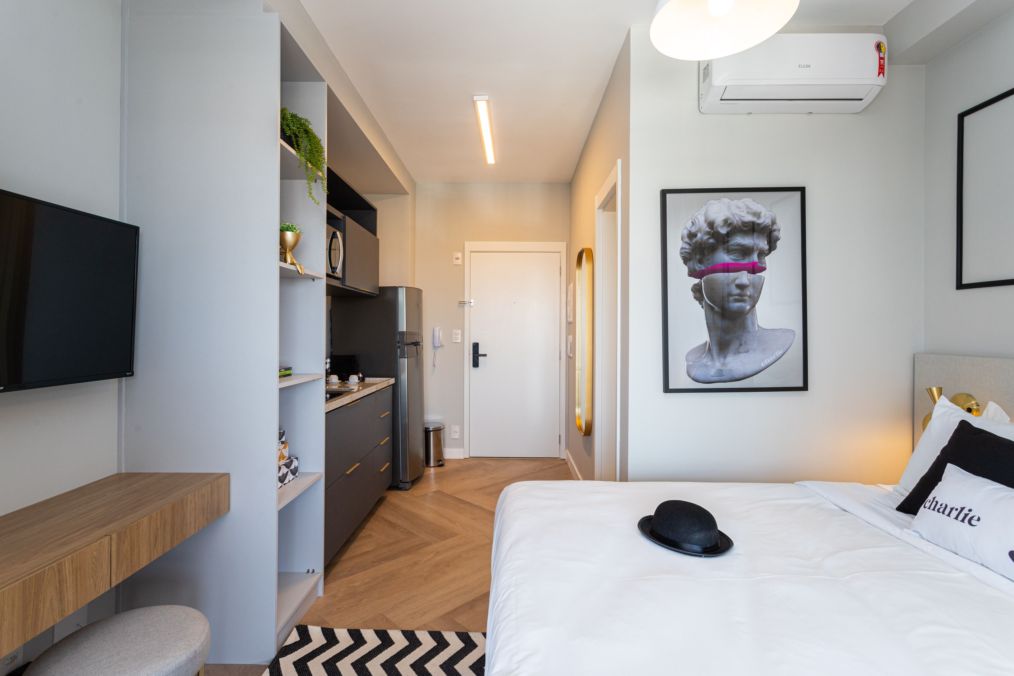 A modern hotel room with a bed, a flat-screen TV, a desk, and a kitchenette.