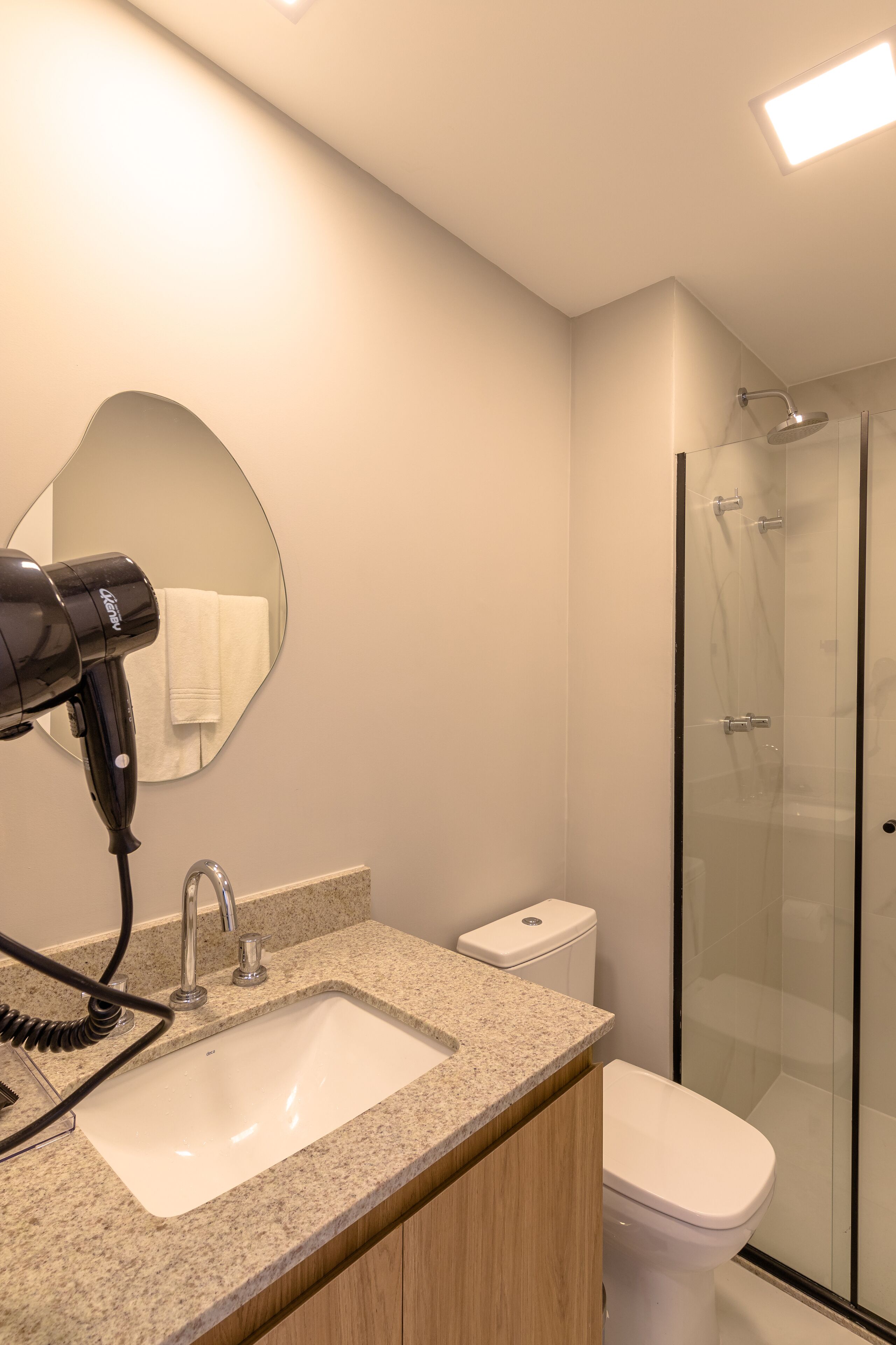 A modern bathroom with a granite countertop sink, a hairdryer, a toilet, and a glass shower enclosure.