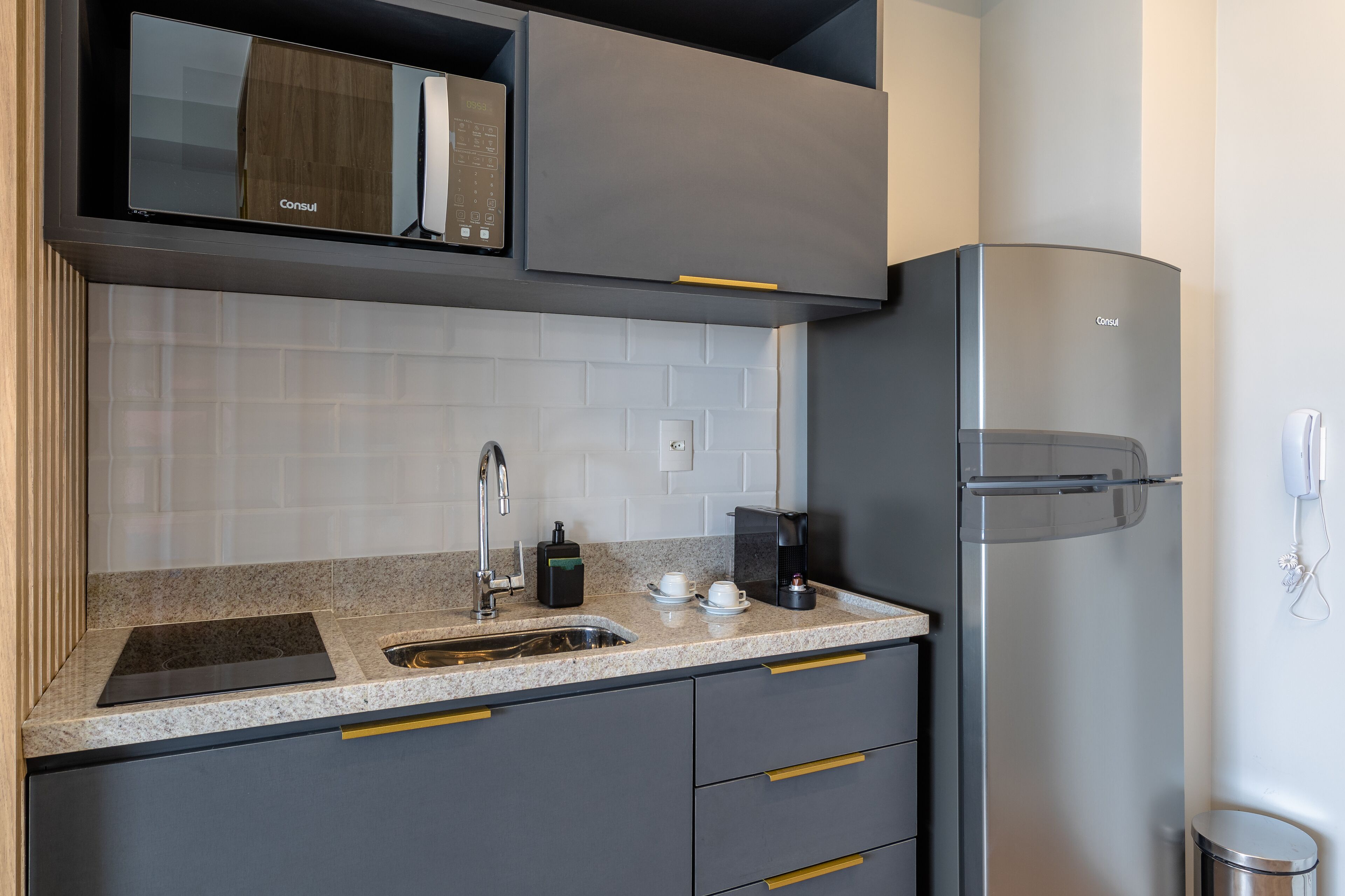 Una cocina moderna con gabinetes grises, un refrigerador de acero inoxidable, un microondas integrado y una encimera de granito.
