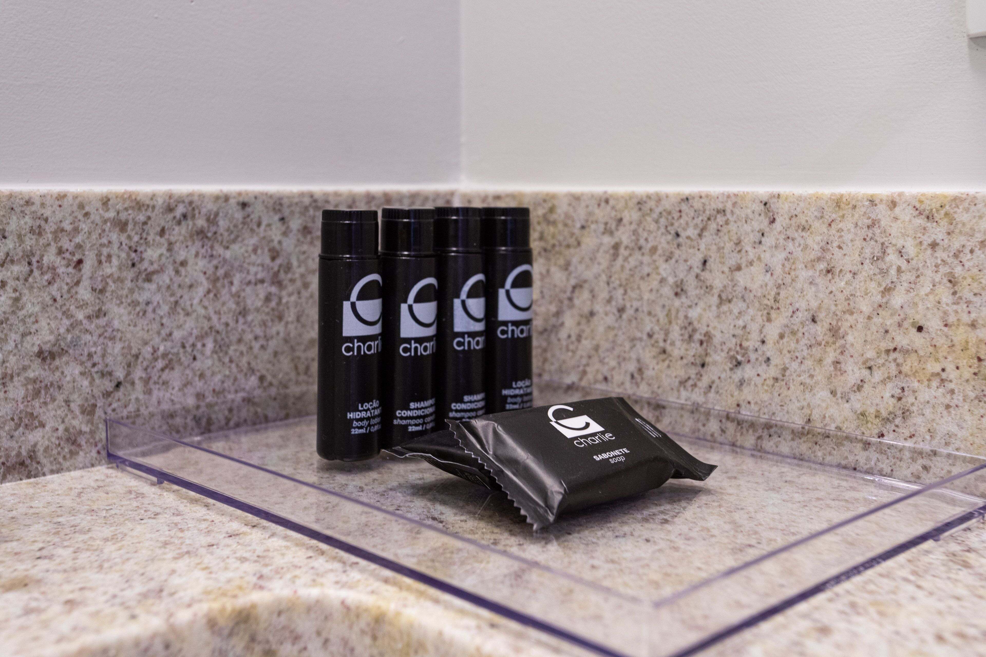 Una encimera de baño con tres botellas de loción corporal 'charlie' y un paquete de champú 'charlie'.