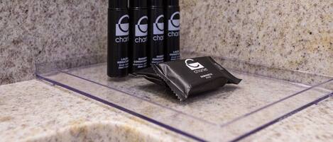 Una encimera de baño con tres botellas de loción corporal 'charlie' y un paquete de champú 'charlie'.