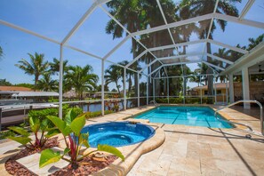 Una piscina exterior cubierta con jacuzzi, rodeada de palmeras y un cielo azul despejado.
