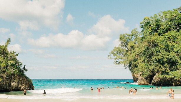 Una playa con aguas turquesas cristalinas, acantilados rocosos y exuberante vegetación.
