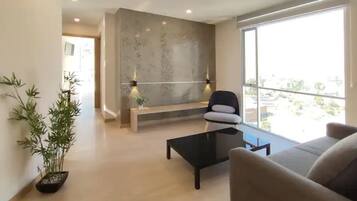 A modern living room with a sofa, a coffee table, and a bench. There is a large window providing a view of the outside.