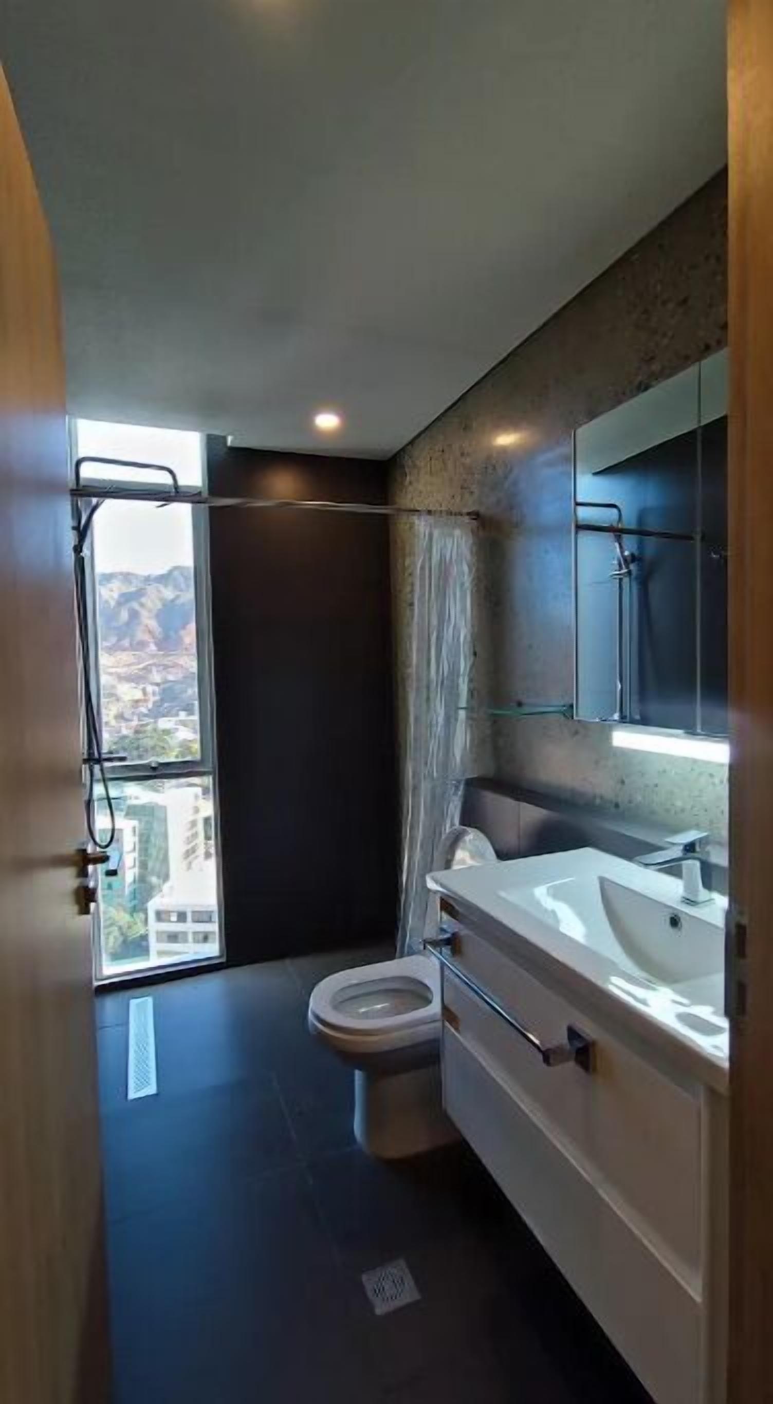 A modern bathroom with a large window, a shower, and a sink.