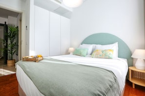 Un lit bien fait, avec une tête de lit verte, une table de chevet avec une lampe et un plateau contenant des éléments pour le petit-déjeuner.