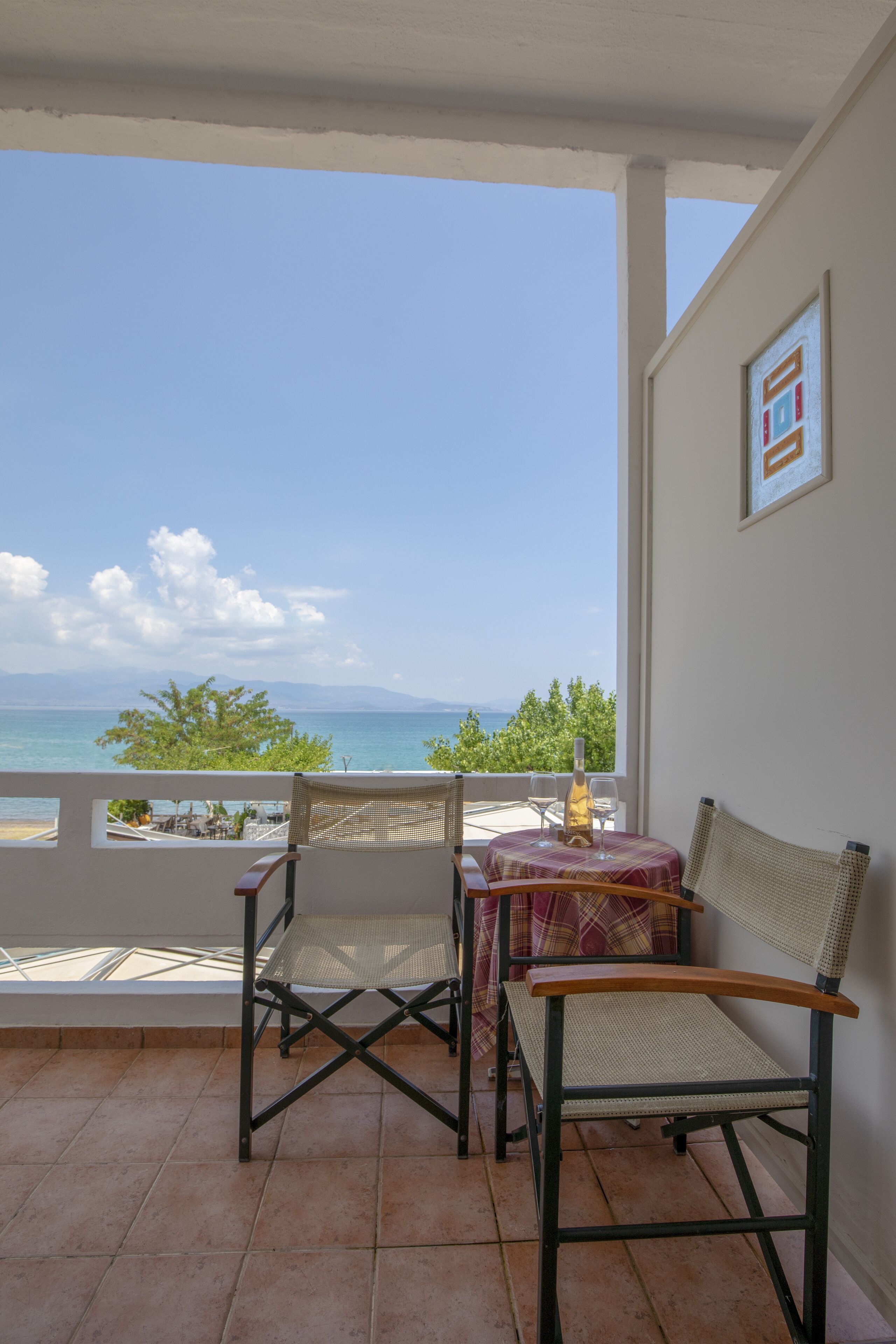 A balcony with a table and chairs, overlooking a scenic view of the sea and mountains.