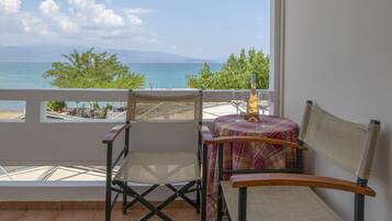 A balcony with a table and chairs, overlooking a scenic view of the sea and mountains.