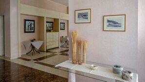 A hotel lobby with a checkered floor, framed pictures on the wall, a reception desk, and a glass display case with decorative items. - Hotel Kypreos Kamena Vourla (Kamena Vourla)