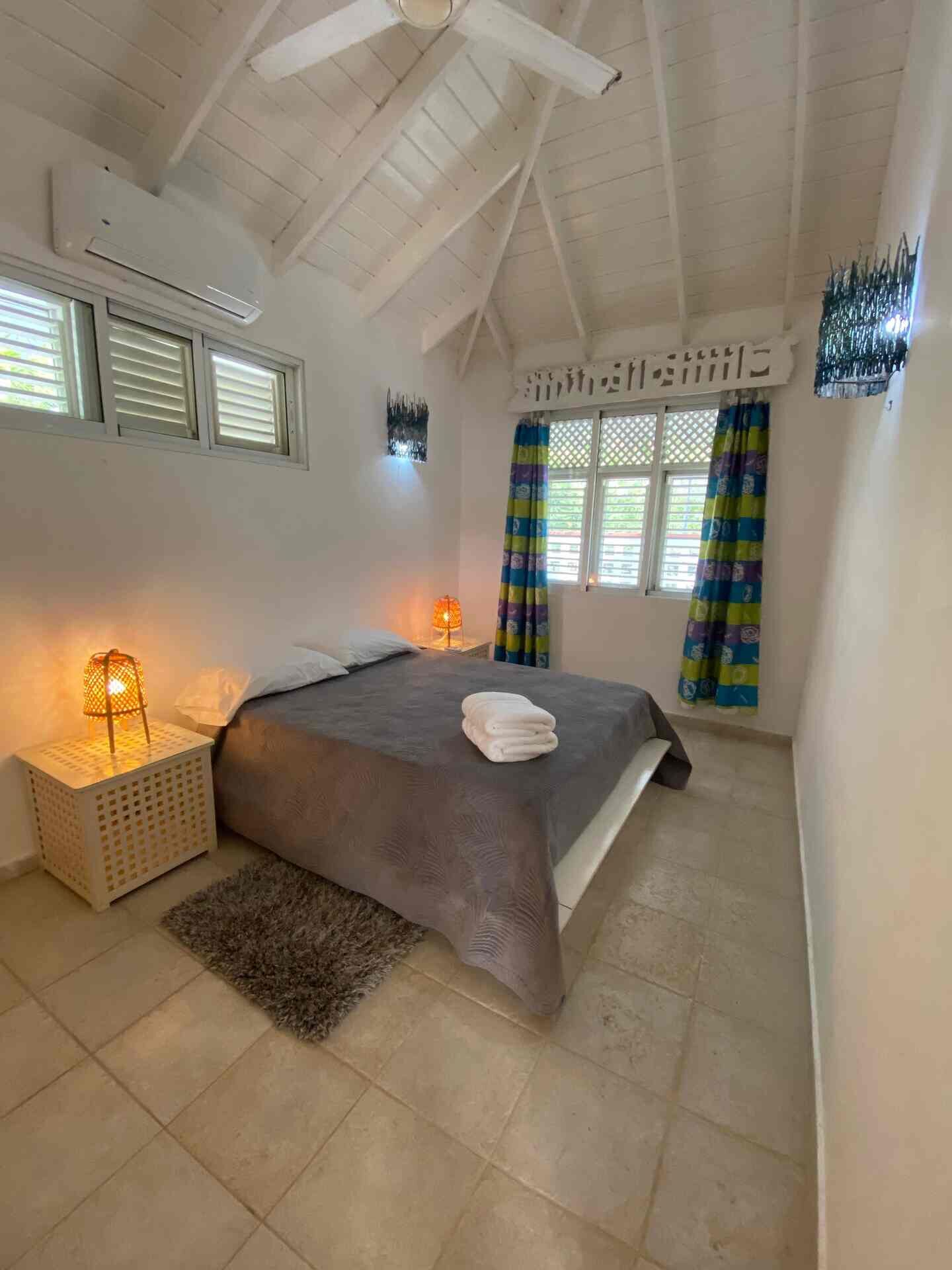 A bedroom with a bed, bedside lamps, a rug, and curtains.