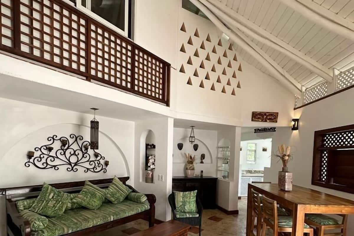 A spacious living area with a high ceiling, a wooden bench, a sofa with green cushions, and a dining table with chairs.