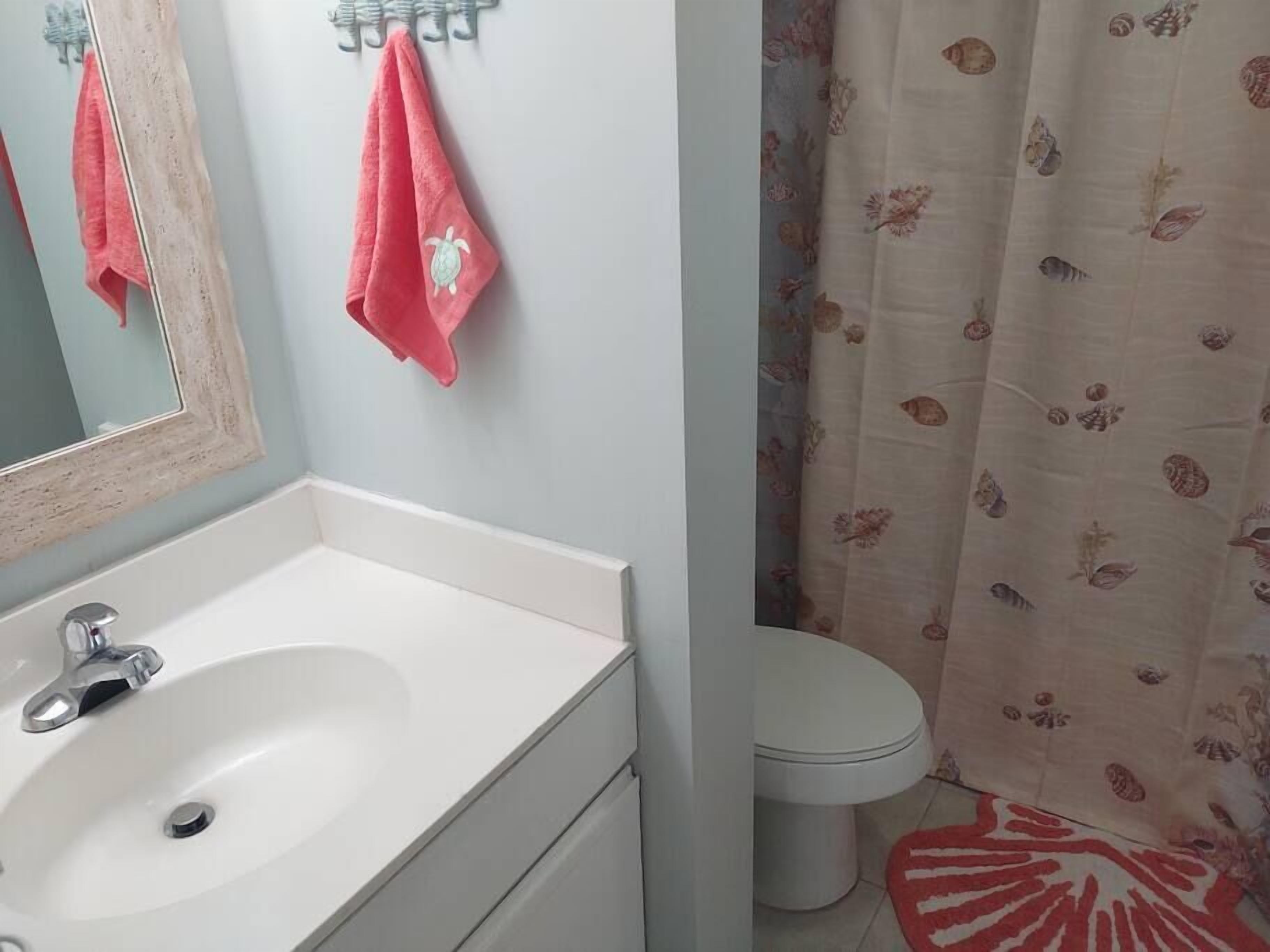 Un bagno con lavandino bianco, uno specchio, un water e una tenda da doccia con motivo floreale.