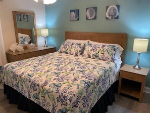 Une chambre à coucher avec une couvre-lit à motifs floraux, une tête de lit en bois, une table de chevet avec une lampe et une commode avec un miroir.
