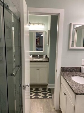 Une salle de bain dotée d’une douche à parois de verre, d’un lavabo avec un plan de travail en granit et d’un carrelage décoratif.