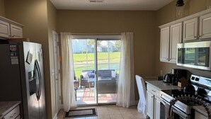 A kitchen with a refrigerator, stove, microwave, and a sliding glass door leading to a patio.