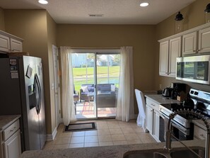 A kitchen with a refrigerator, stove, microwave, and a sliding glass door leading to a patio.