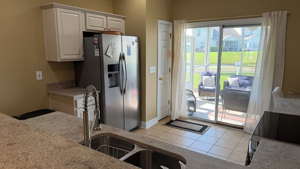 A kitchen with a stainless steel refrigerator, a sink with soap dispensers, and a sliding glass door leading to a patio area.