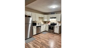A kitchen with white cabinets, stainless steel appliances, and a patterned rug. - NEW 39th Street hot tub (Oklahoma City)