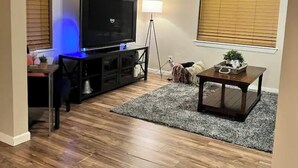 A living room with a flat-screen TV, a standing lamp, a coffee table, and a rug. - NEW 39th Street hot tub (Oklahoma City)