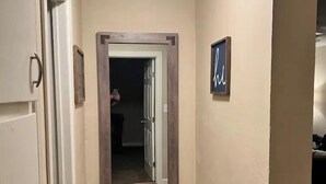 A hallway with a wooden floor, a door on the left, and a framed picture on the wall. - NEW 39th Street hot tub (Oklahoma City)