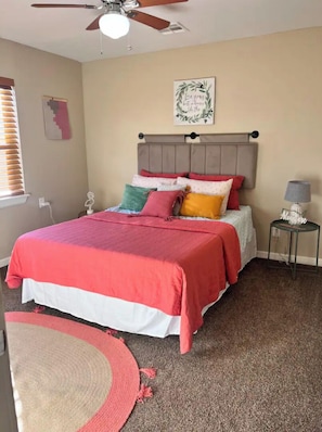 Una camera da letto con un letto, un ventilatore a soffitto, un comodino con una lampada e una decorazione a parete.