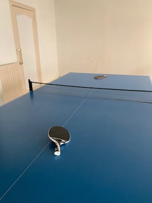 Une table de ping-pong avec une raquette au premier plan et une porte en arrière-plan.
