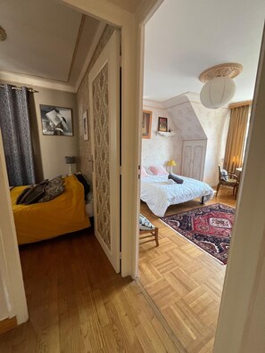A bedroom with a bed, a yellow sofa, a patterned wall, and a wooden floor.