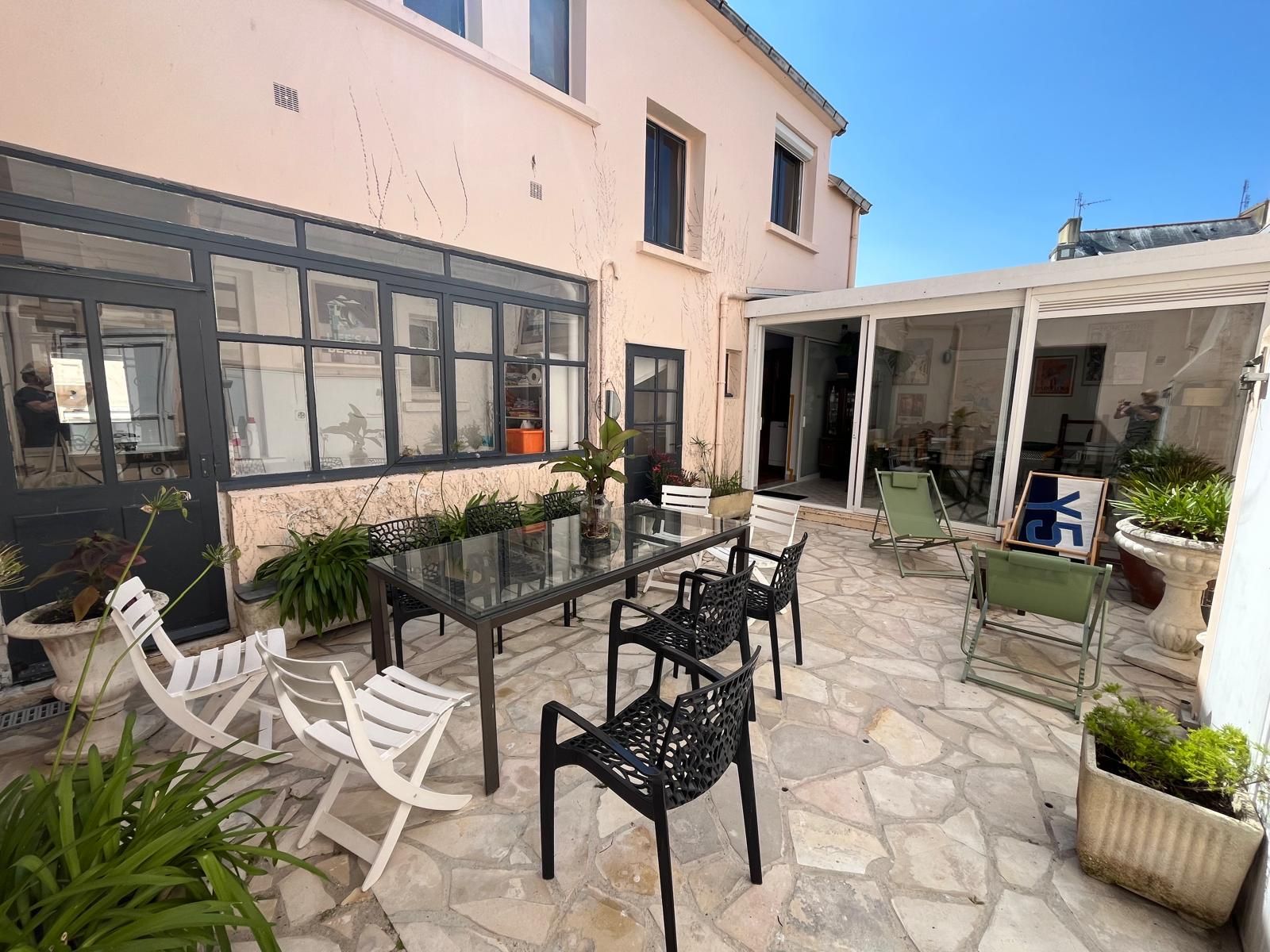 Une terrasse avec une table et des chaises en verre, entourée de plantes en pot et dotée d’un sol en pierre.