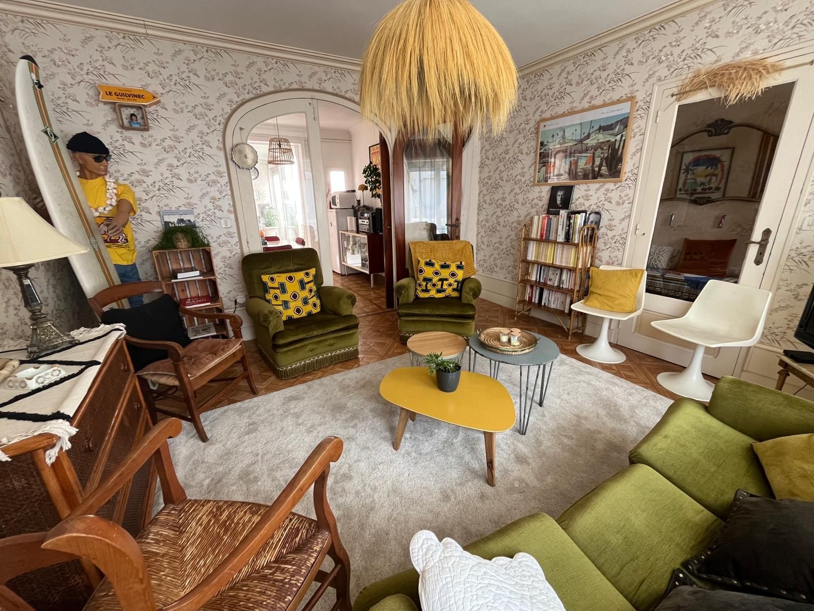 Ein gemütliches Wohnzimmer mit einem grünen Sofa, einem Holztisch und einem Bücherregal voller Bücher.