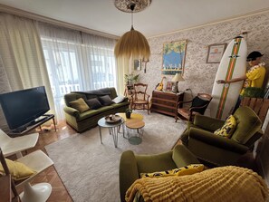 A living room with a sofa, chairs, a coffee table, a TV, and a surfboard. - The harbor and beaches are within walking distance; a surfing and kitesurfing spot is 10 minutes away (Guilvinec)