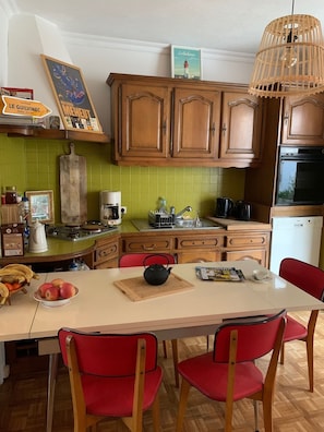 Une cuisine avec des meubles en bois, un plan de travail blanc, un revêtement mural en carreaux verts et un coin repas avec des chaises rouges.