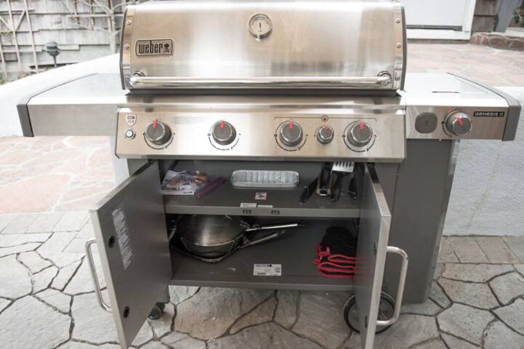 Un barbecue à gaz Weber Genesis II en acier inoxydable, doté de quatre brûleurs, d’une étagère latérale et d’un thermomètre intégré.