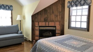 A bedroom with a fireplace, a sofa, a bed, and a window with blinds. - Baladerry Inn (Gettysburg)