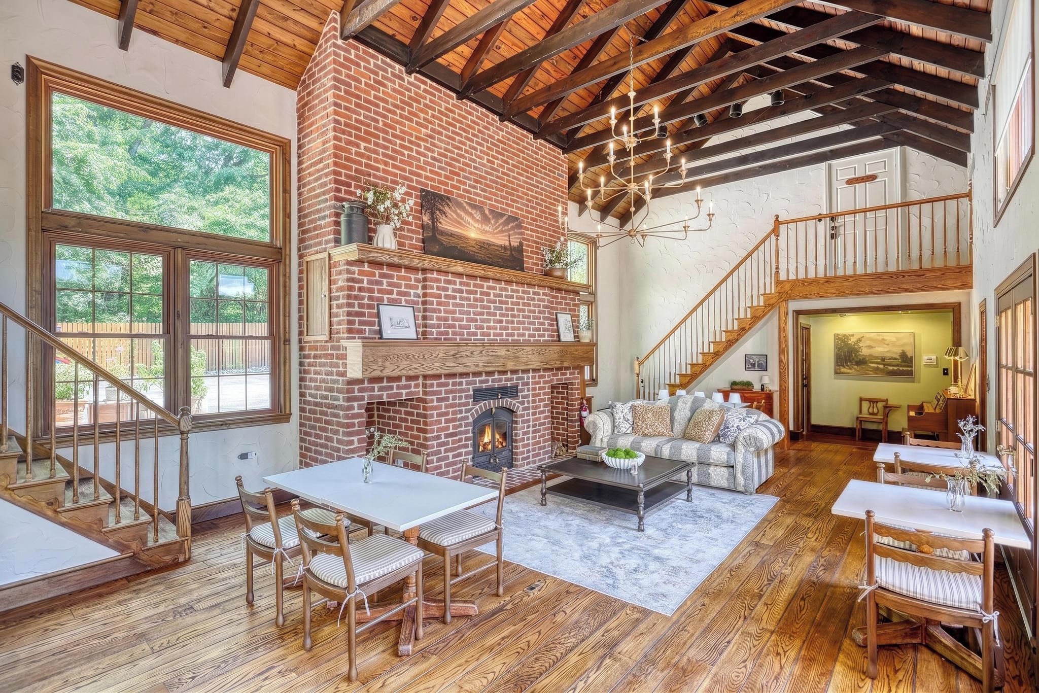 A spacious living area with a brick fireplace, wooden flooring, and a staircase leading to an upper level.