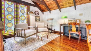 Una habitación acogedora con techo de madera, una ventana de vitral, chimenea y un rincón de descanso con alfombra.