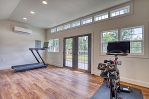 Un gimnasio en casa con cinta de correr, bicicleta estática y televisor montado en la pared.