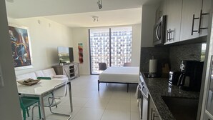A modern kitchen with a large window, a dining area with a table and chairs, and a bedroom with a bed. - Studio Unit at Downtown Doral (Doral)
