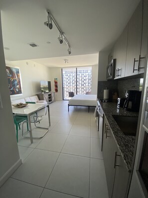 Une cuisine moderne dotée d’une grande fenêtre, un coin repas avec une table et des chaises, et une chambre à coucher avec un lit.