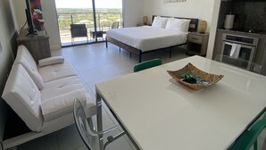 A modern hotel room with a balcony, a bed, a dining table, and a kitchenette. - Studio Unit at Downtown Doral (Doral)