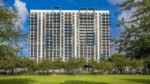 A multi-story building with a modern architectural design, surrounded by a well-maintained grassy area and trees. - Studio Unit at Downtown Doral (Doral)