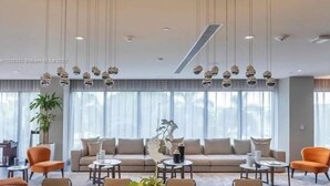 A modern living room with a sofa, orange chairs, and hanging spherical light fixtures. - Studio Unit at Downtown Doral (Doral)