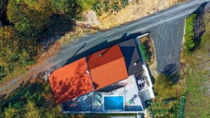 Vista aérea de una casa moderna con techo rojo, piscina y un amplio ventanal de vidrio.