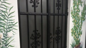 Una reja de metal negro con detalles decorativos, una pared con un mural de plantas y un suelo de baldosas.