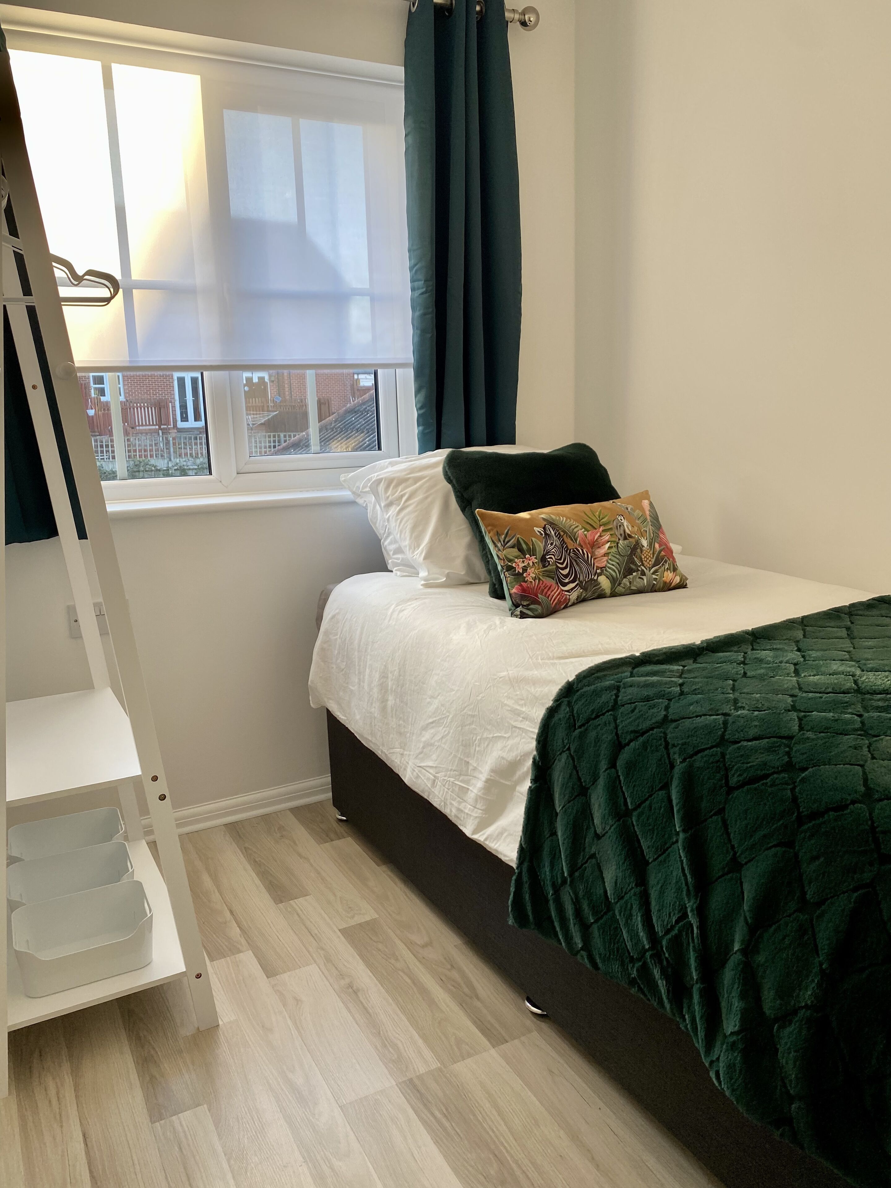 Un dormitorio con cama, ventana con cortinas, una estantería blanca y vistas al exterior.